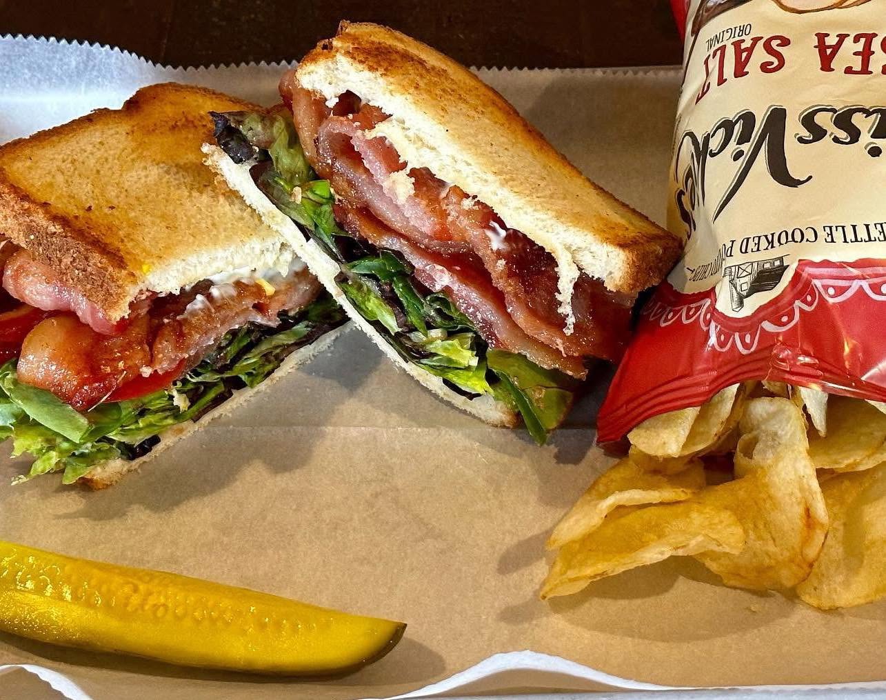 Toasted bacon, lettuce and tomato sandwich with chips and a pickle