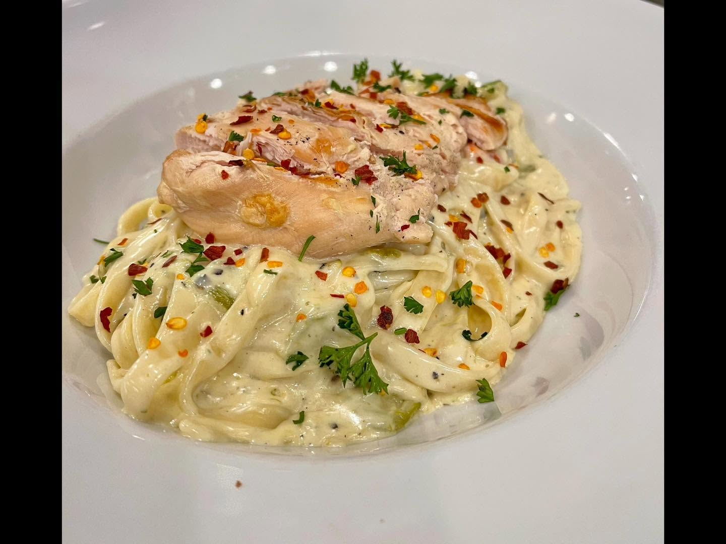 Fettuccine alfredo topped with sliced chicken and chile flakes