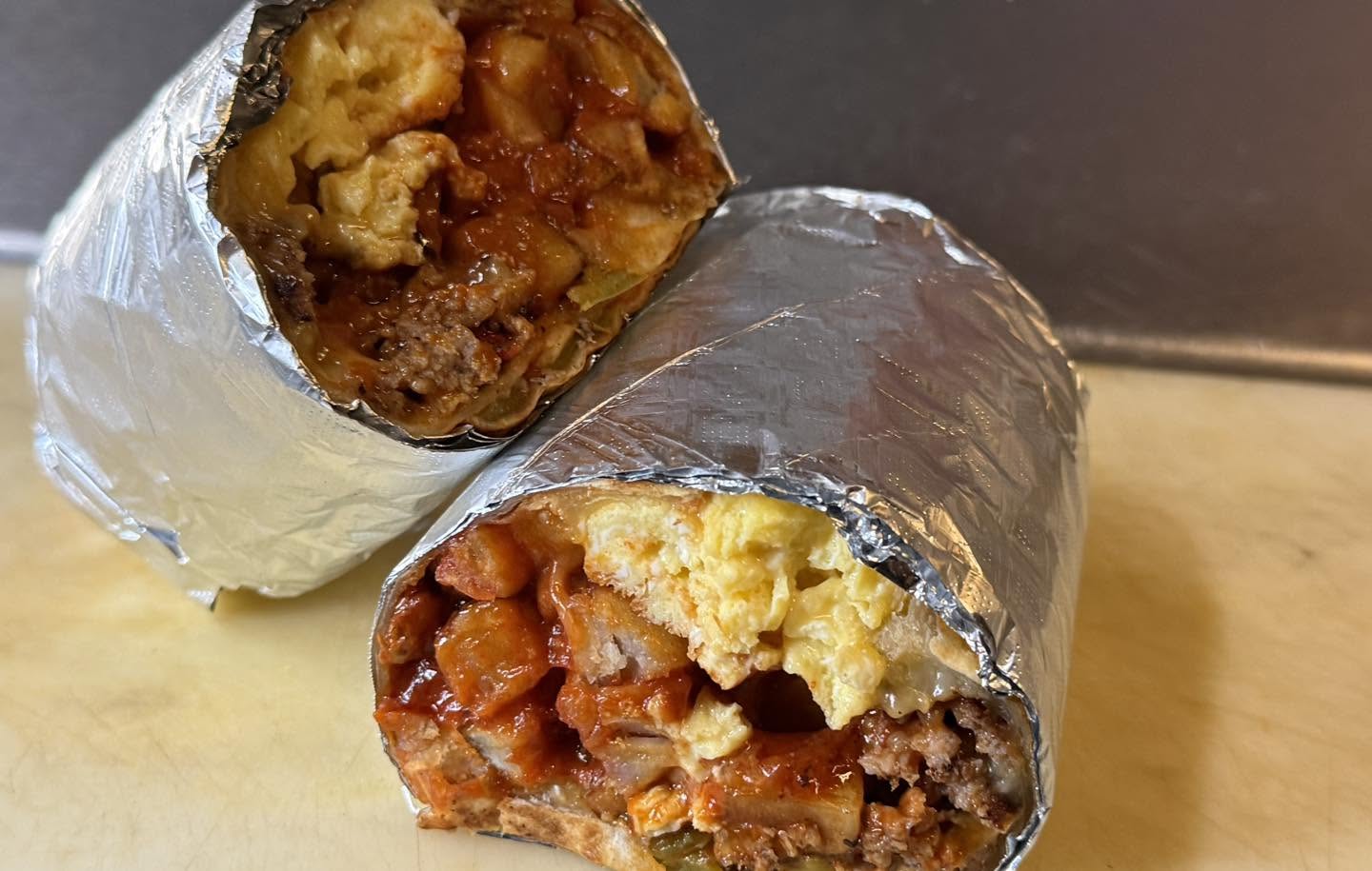 Foil-wrapped breakfast burrito cut open with egg, potato and red chile